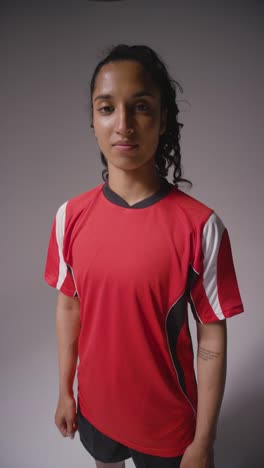 Vertical-Video-Studio-Shot-Of-Female-Footballer-Wearing-Club-Kit-Against-Grey-Background-Catching-Ball-1